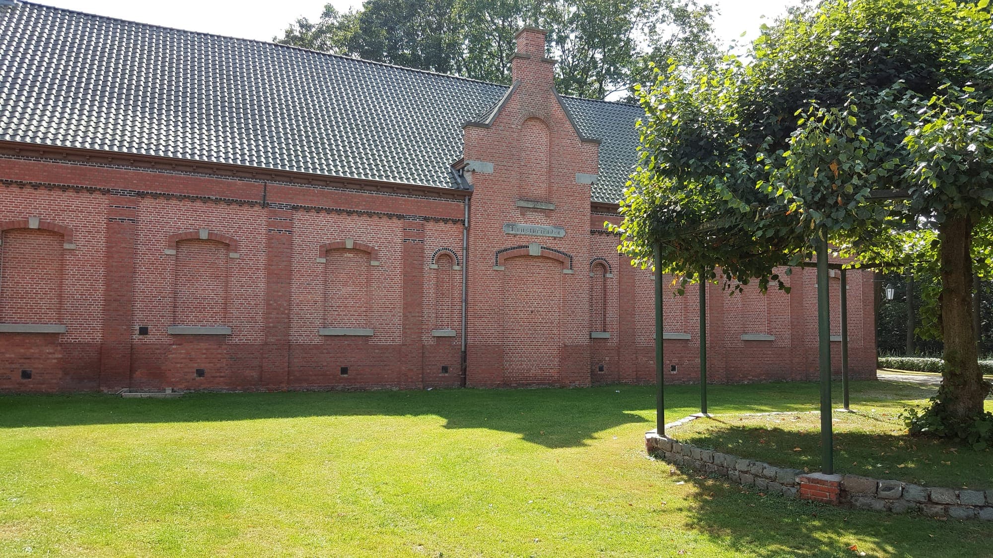 De zijgevel van de zaal met het grasveld ernaast